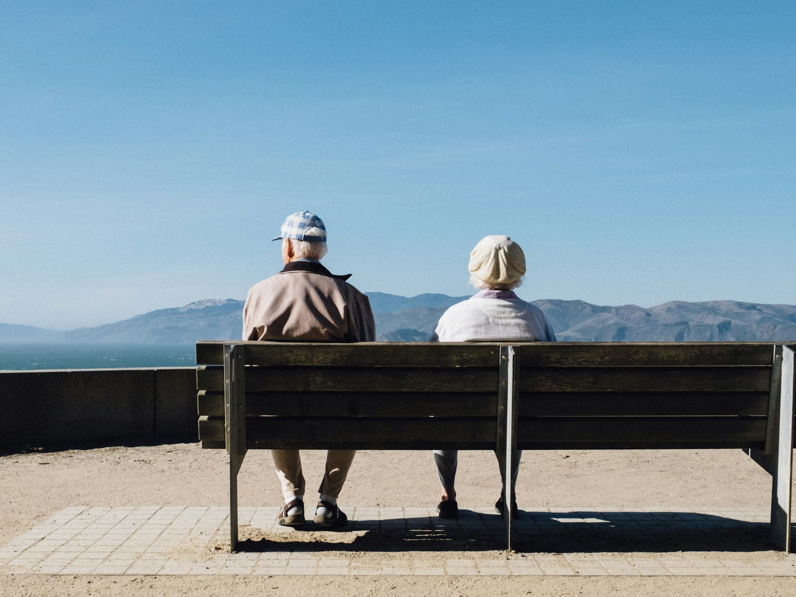 An older couple resting on a bench by the sea